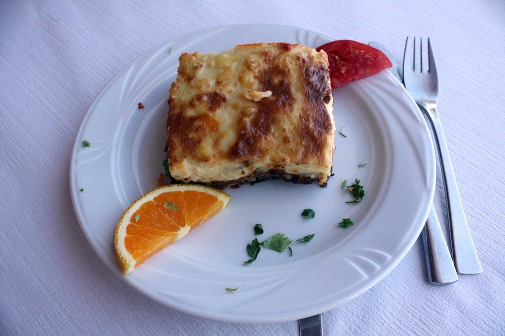 Slice of moussaka with a golden béchamel top on a white plate with an orange wedge