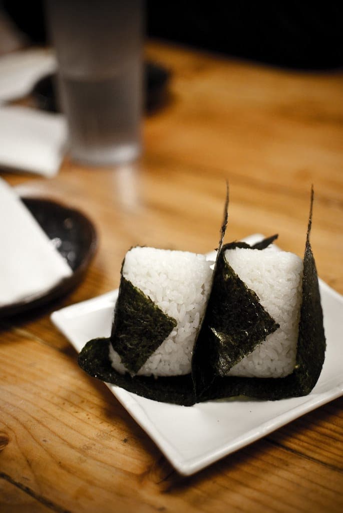 Two triangular onigiri rice balls wrapped in nori on a small white plate