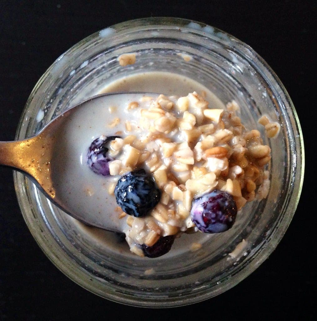 A spoonful of creamy overnight oats with blueberries lifted from a glass jar