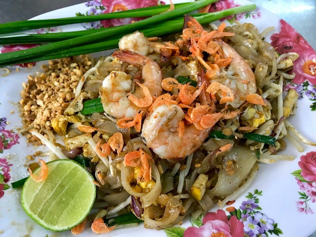 Shrimp pad thai with dried shrimp, bean sprouts, chives, peanuts and a lime half on a floral plate