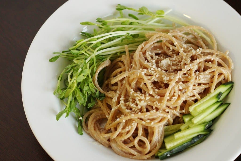 Peanut sesame noodles with cucumber sticks and pea shoots on a white plate