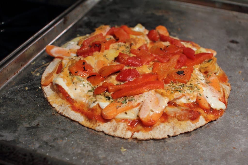 Pita pizza topped with tomato sauce, melted cheese and roasted red peppers on a baking tray