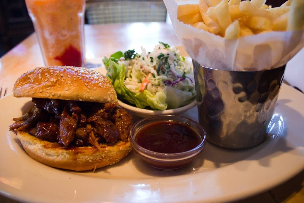 Pulled pork sandwich on a sesame bun with fries, coleslaw and a cup of barbecue sauce