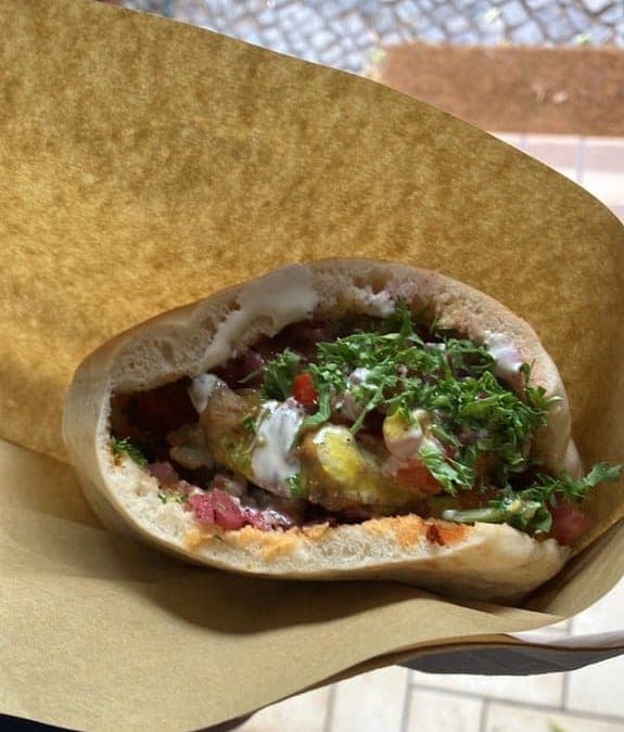 Pita stuffed with sabich fillings, chopped salad and herbs, wrapped in paper