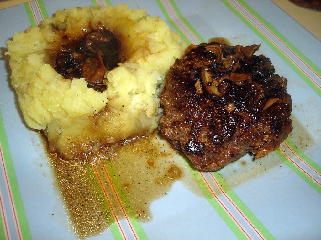 Beef patty in mushroom gravy beside a mound of mashed potatoes