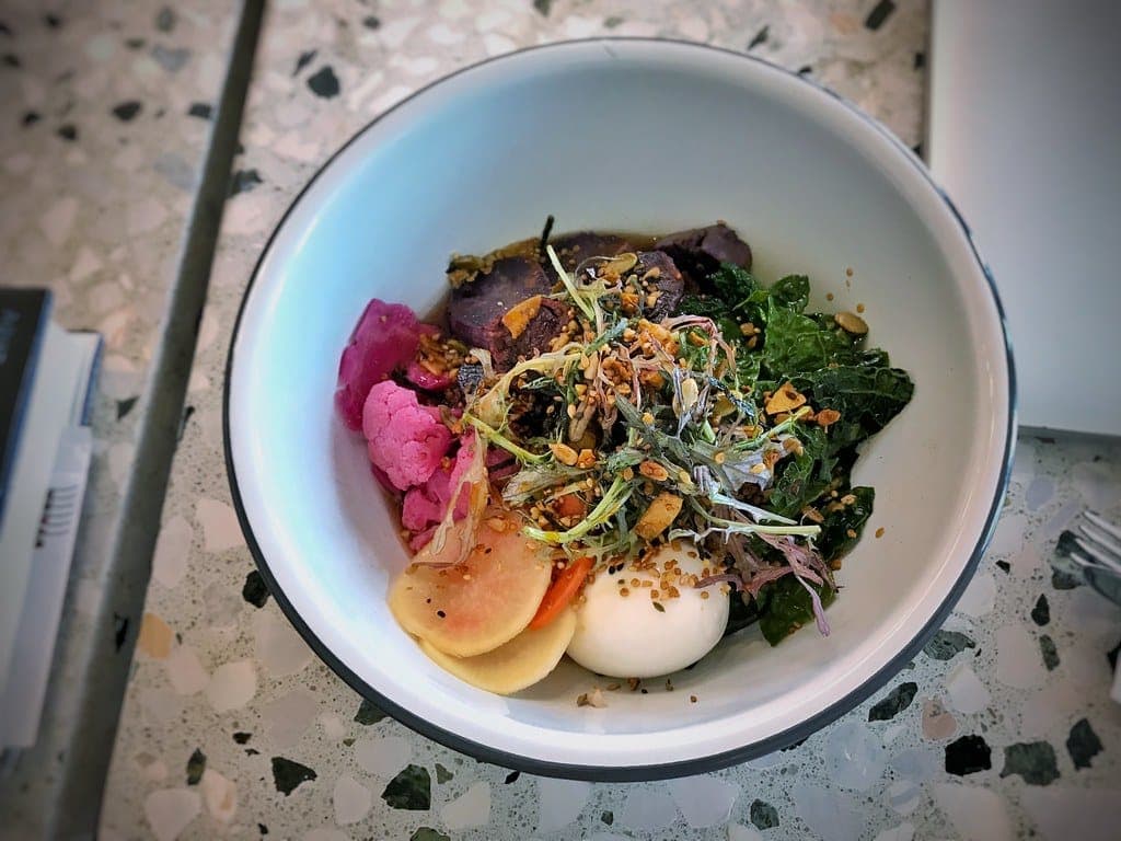 A savoury grain bowl topped with a soft-boiled egg, greens, sprouts and pickled onion