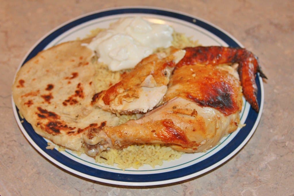 Roasted chicken leg with golden skin over rice with flatbread and a spoonful of yogurt sauce