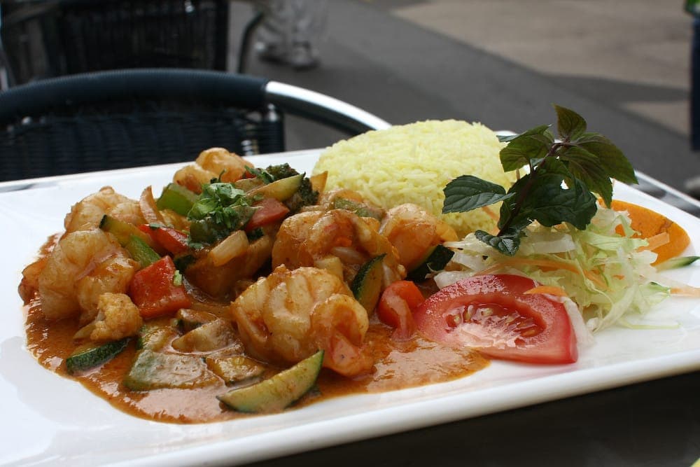 Shrimp curry with zucchini and tomato in an orange sauce, with yellow rice and salad