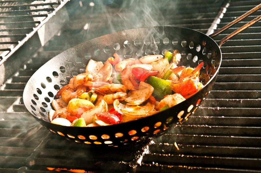Shrimp, peppers and onions sizzling in a grill basket over an open flame