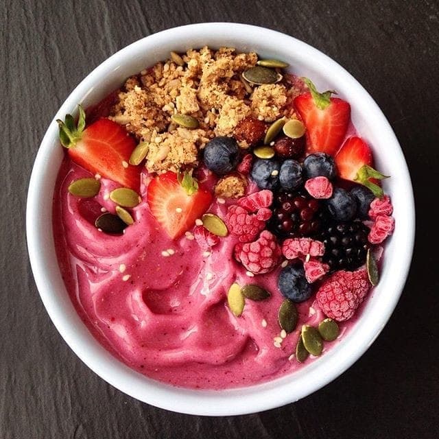 A bright pink smoothie bowl topped with strawberries, blackberries, raspberries and granola