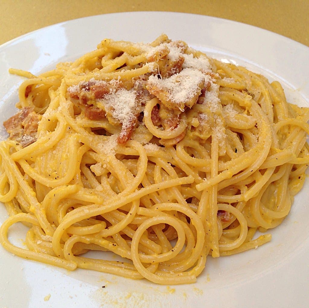 A plate of spaghetti carbonara coated in a glossy yellow egg sauce with crisp pieces of pork and grated pecorino