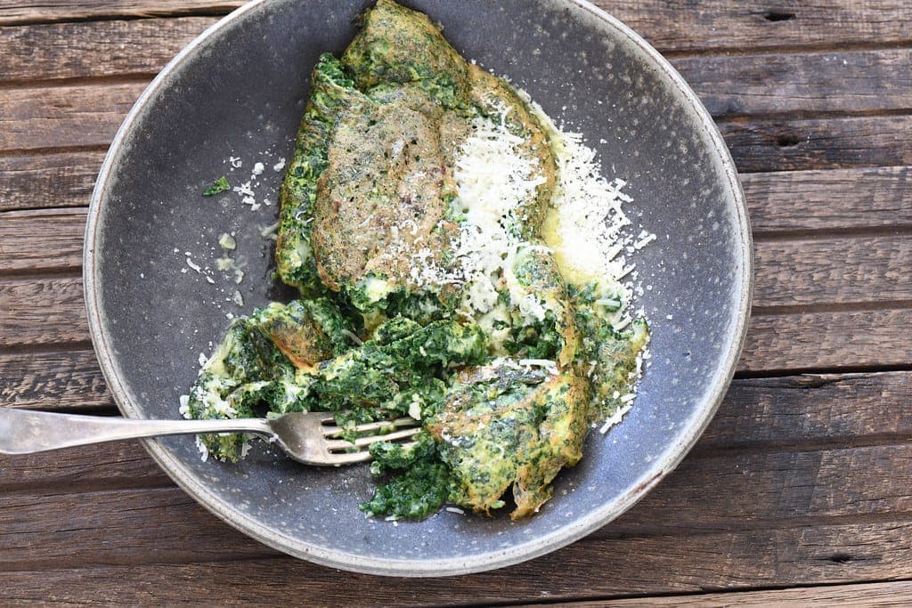 A folded green spinach omelette dusted with grated cheese in a grey bowl