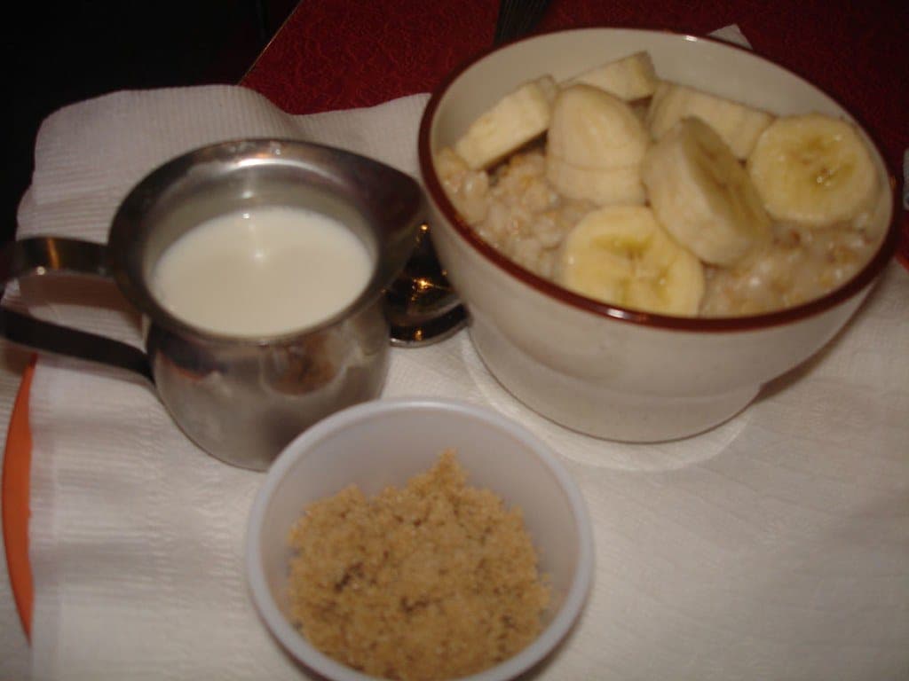 A bowl of steel cut oatmeal topped with sliced banana, with milk and brown sugar on the side
