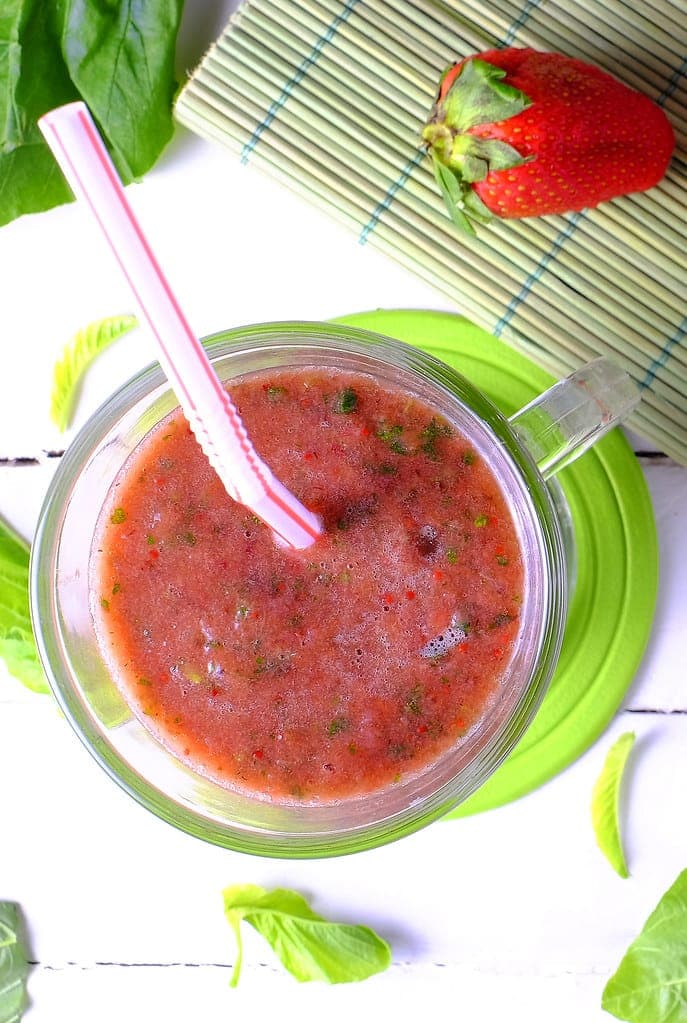 A red strawberry smoothie with a pink straw in a glass