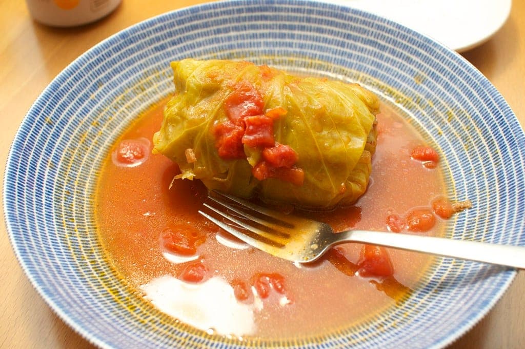 Stuffed cabbage roll in tomato sauce in a blue striped bowl with a fork