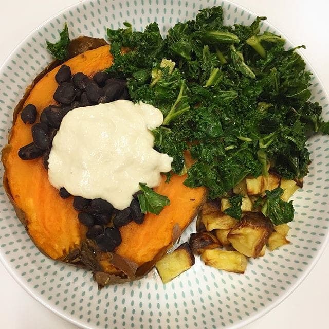 Baked sweet potato topped with black beans and a creamy sauce beside sautéed kale