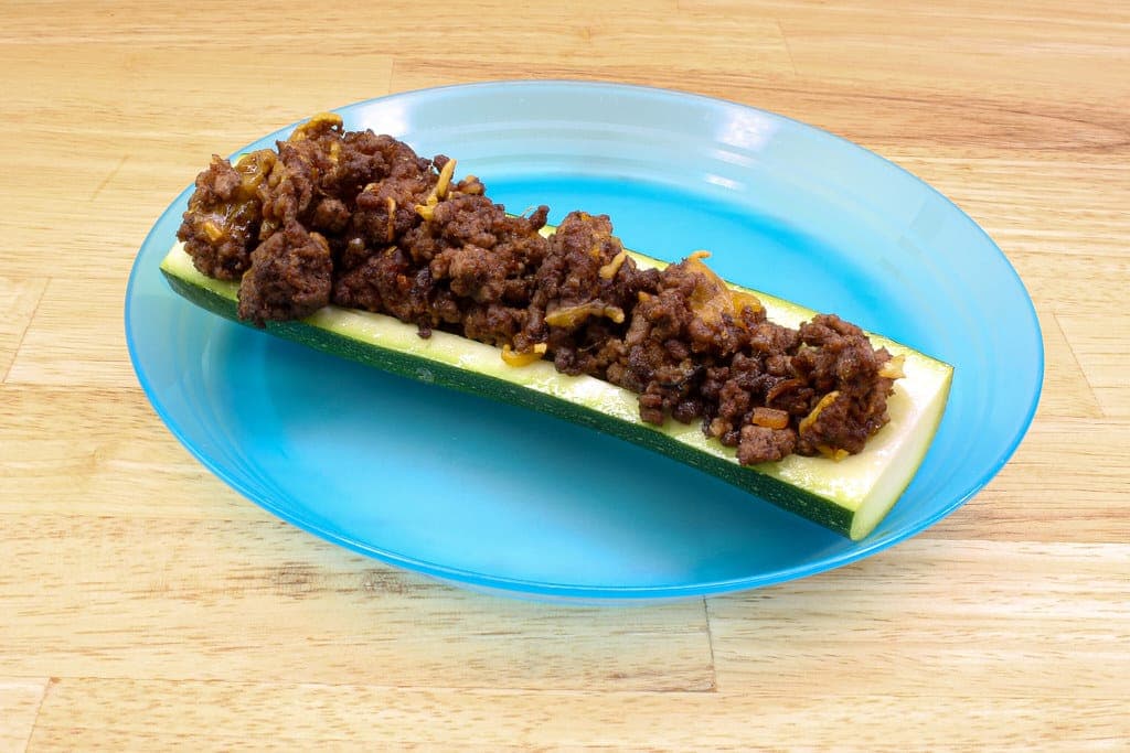 Zucchini half filled with browned ground meat on a blue plate