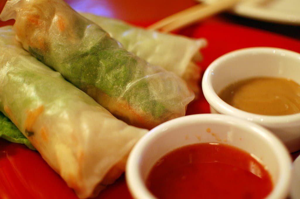 Fresh rice paper summer rolls with dipping sauces on a red plate