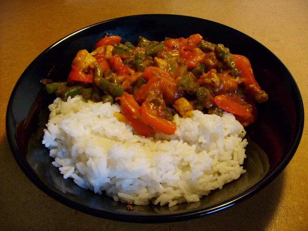 Bowl of red curry with green beans and red pepper over steamed white rice