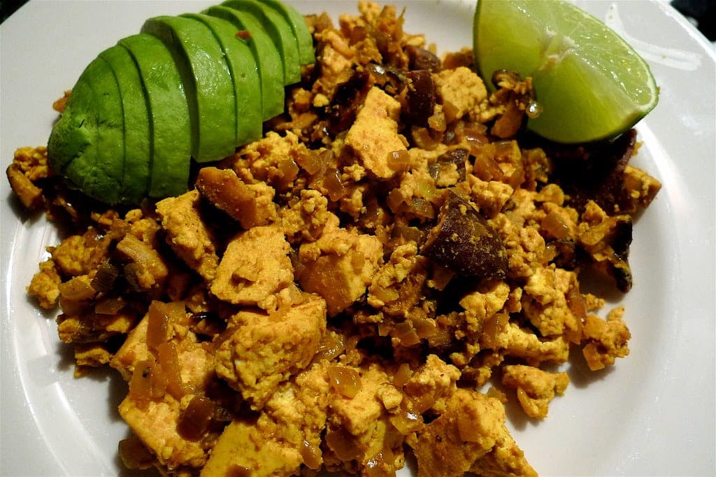 Golden turmeric tofu scramble served with sliced avocado and a lime wedge