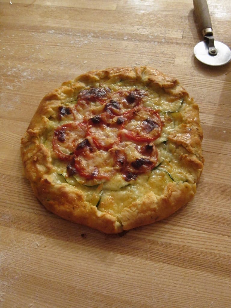 Rustic free-form galette with a folded golden crust and roasted tomato slices on a wooden board