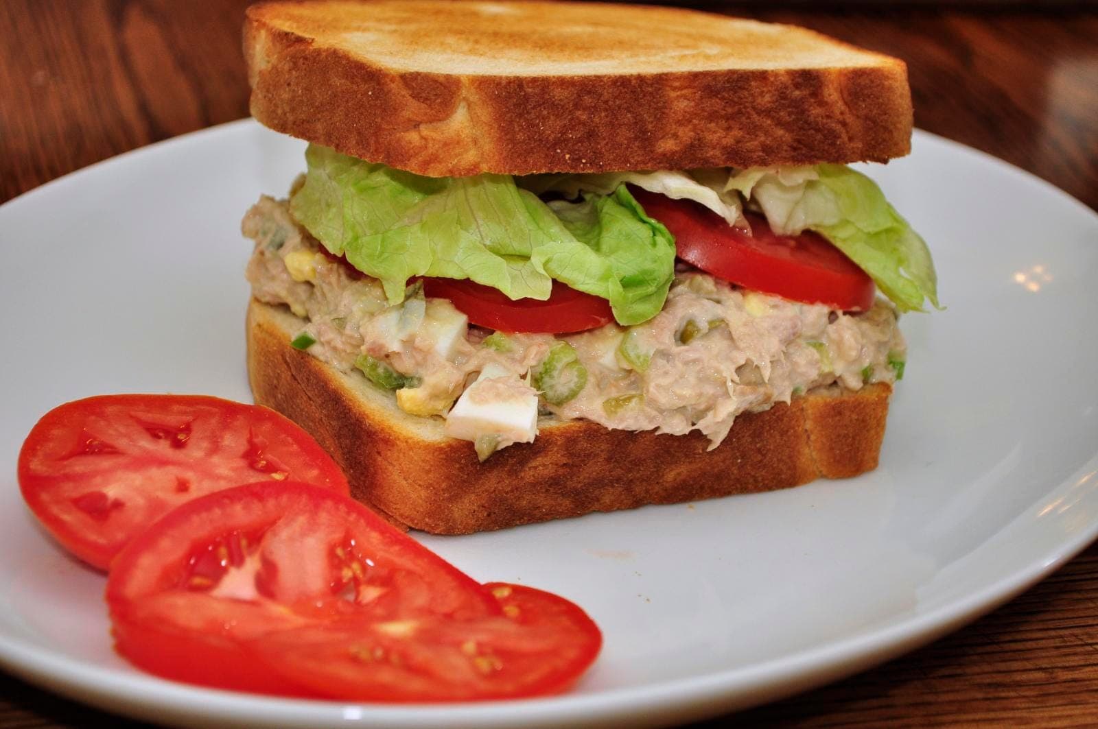 Tuna salad sandwich on toasted bread with lettuce and tomato, with extra tomato slices