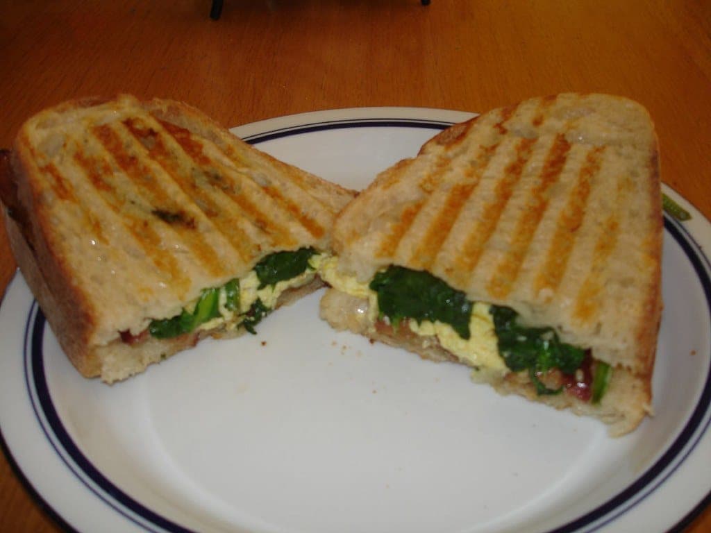Pressed panini with grill marks, cut in half to show a spinach and cheese filling
