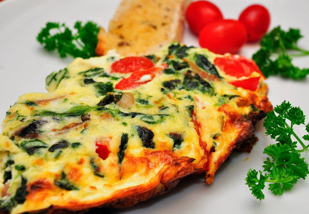 A spinach and tomato frittata garnished with parsley and cherry tomatoes