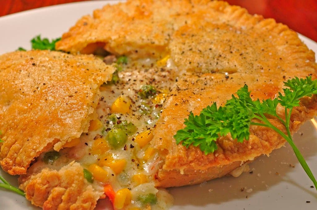 Pot pie with a golden, crimped crust cut open to show a creamy filling with peas and corn