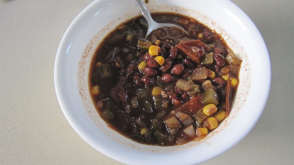 Bowl of black bean chili with corn and peppers with a spoon
