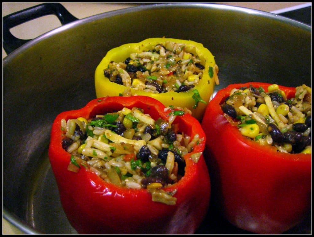 Red and yellow bell peppers stuffed with rice, black beans and corn in a pan