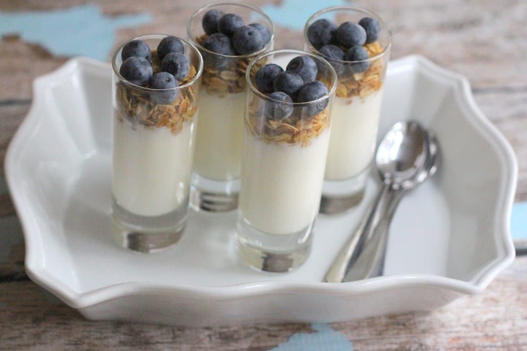 Tall glasses of yogurt parfait layered with granola and topped with blueberries